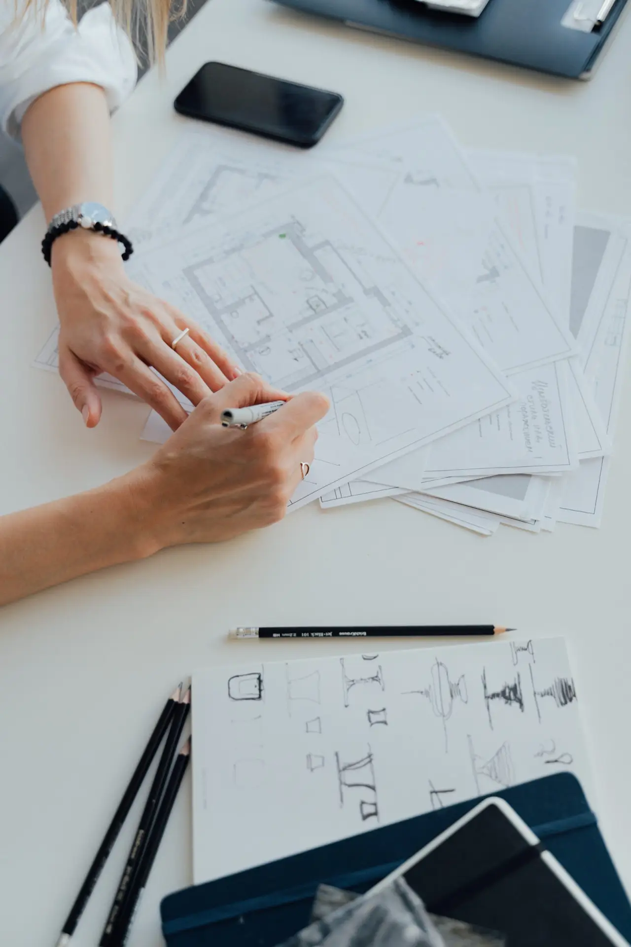Main d'une architecte qui anote, sur son bureau, des plans au format A4.